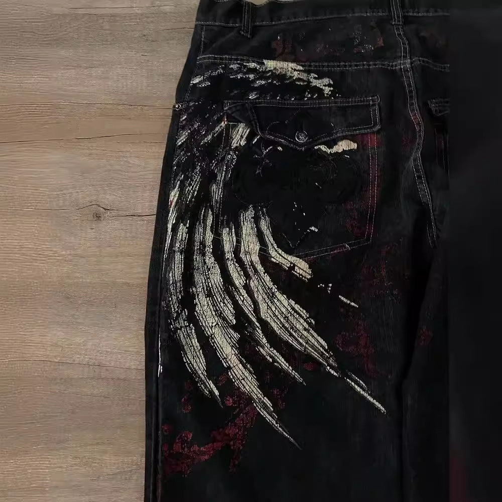 FreyaVibe hip hop jeans close-up — gold brushstroke wing embroidery and red graphic detail on black denim