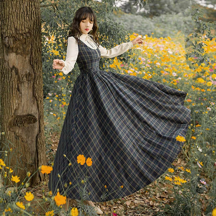 The Countryside Plaid Pinafore Dress FV — model in dark navy tartan pinafore over white blouse, twirling in a wildflower garden
