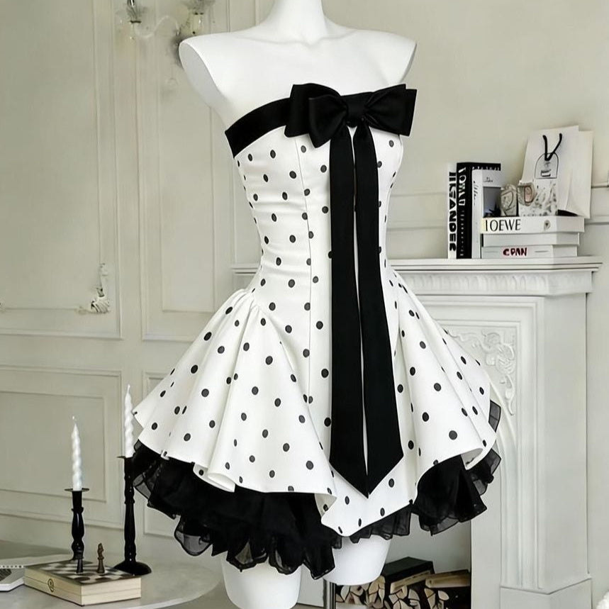 Polka dot strapless mini dress in white and black – front view showing structured bodice, full skirt, black velvet bow and tulle hem
